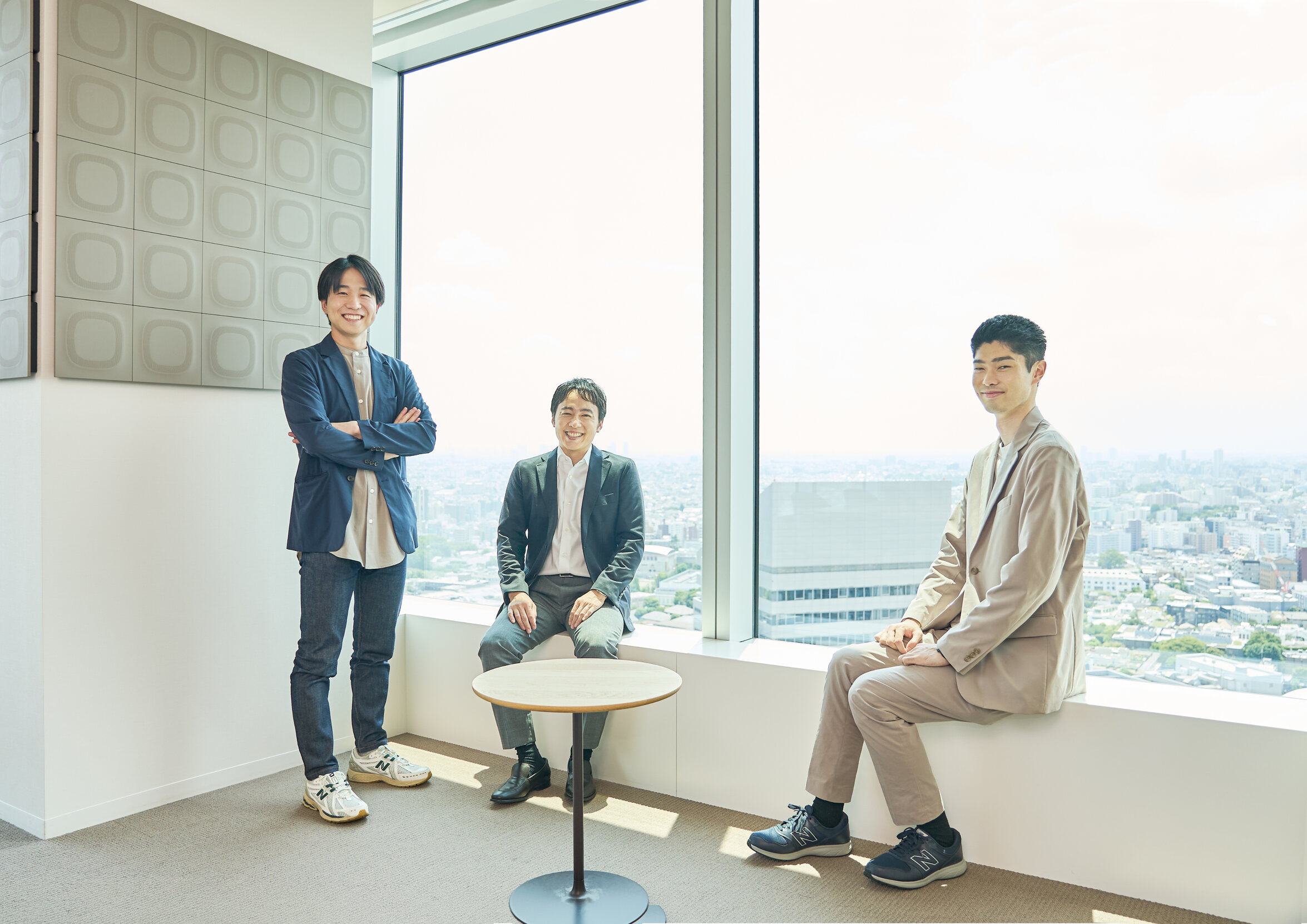 オフィスの窓辺に集まる若手アナリスト3名
